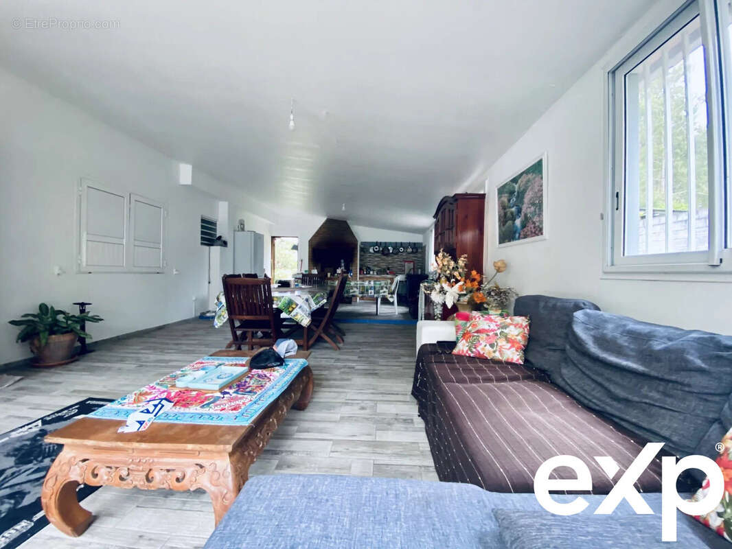 Salle de séjour lumineuse avec un canapé, une table basse en bois, et une table à manger au fond. - Maison à LA PLAINE-DES-PALMISTES