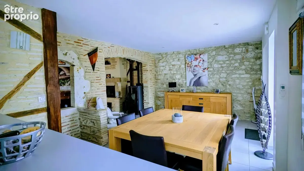 Salle à manger avec murs en pierre apparente, grande table en bois, et décoration intérieure chaleureuse.
