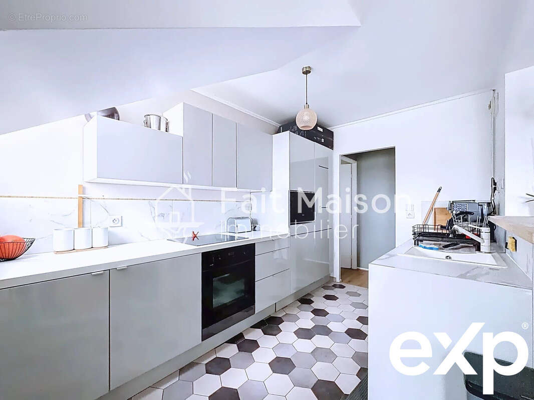 Cuisine moderne avec des armoires blanches, un four encastré, et un sol à carreaux hexagonaux. - Appartement à MASSY