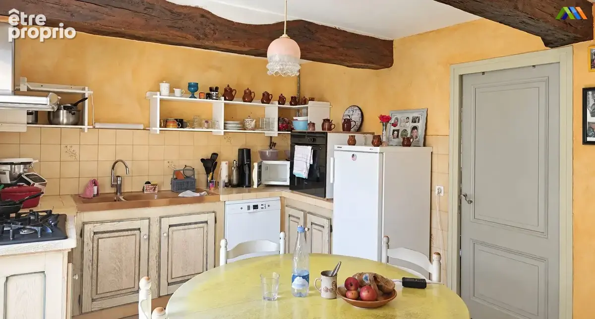 Kitchen with exposed wooden beams, pale cabinetry and a dining table in a traditional house near Montesquiou.