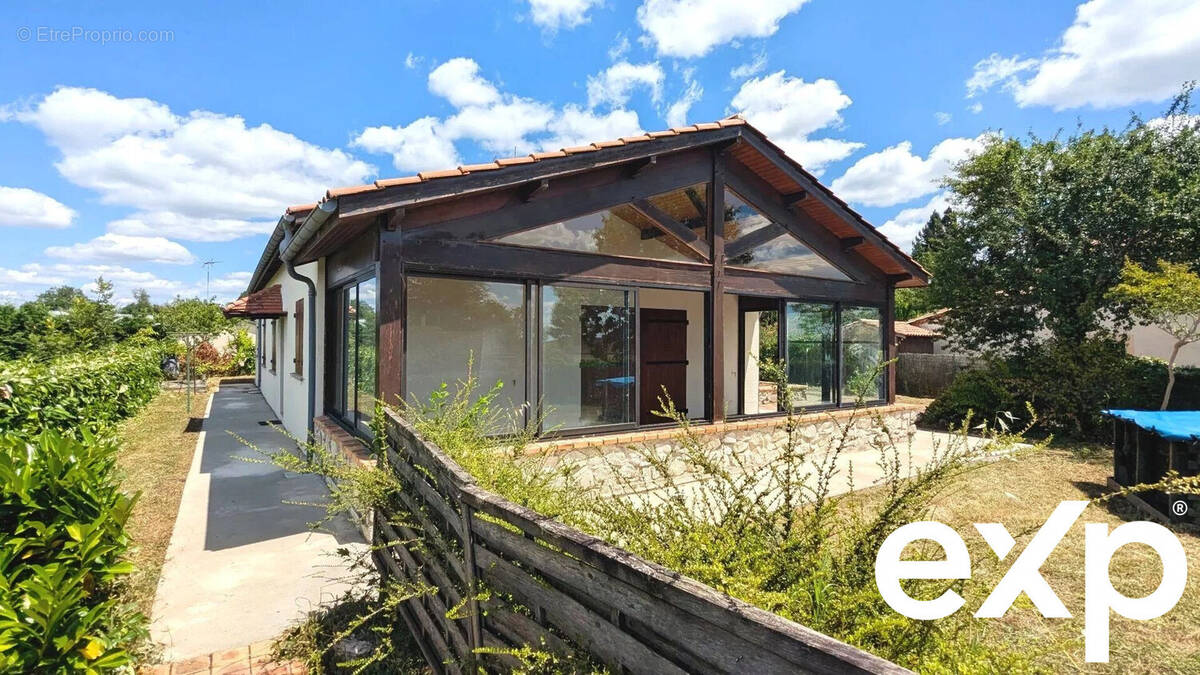 Maison avec de grandes baies vitrées autour de la terrasse, entourée de nature sous un ciel bleu. - Maison à FOULAYRONNES