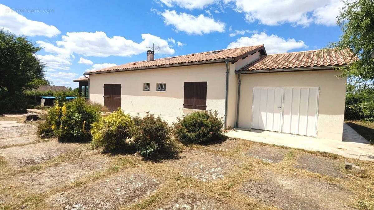 Une maison en quartier résidentiel avec un toit en tuiles, des volets en bois, et un jardin entouré de verdure sous un ciel bleu. - Maison à FOULAYRONNES