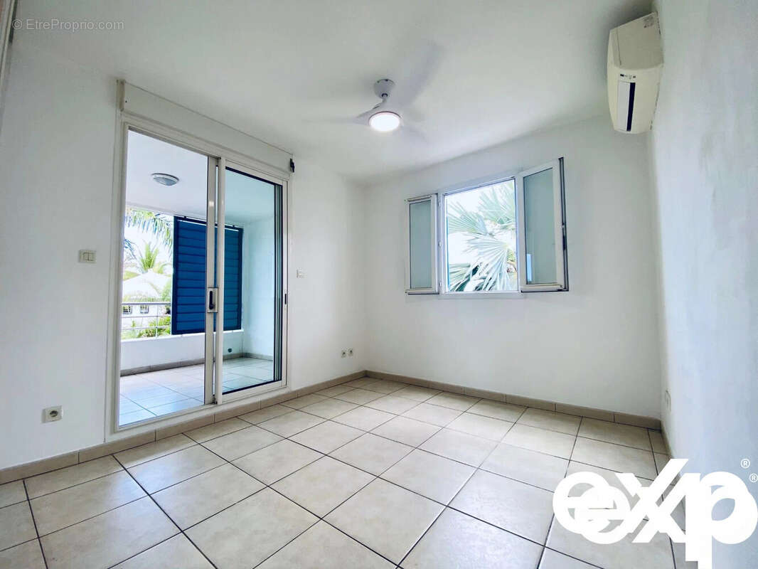 Une pièce lumineuse avec carrelage, un ventilateur au plafond, une fenêtre et une porte-fenêtre donnant sur une terrasse. - Appartement à SAINT-PAUL