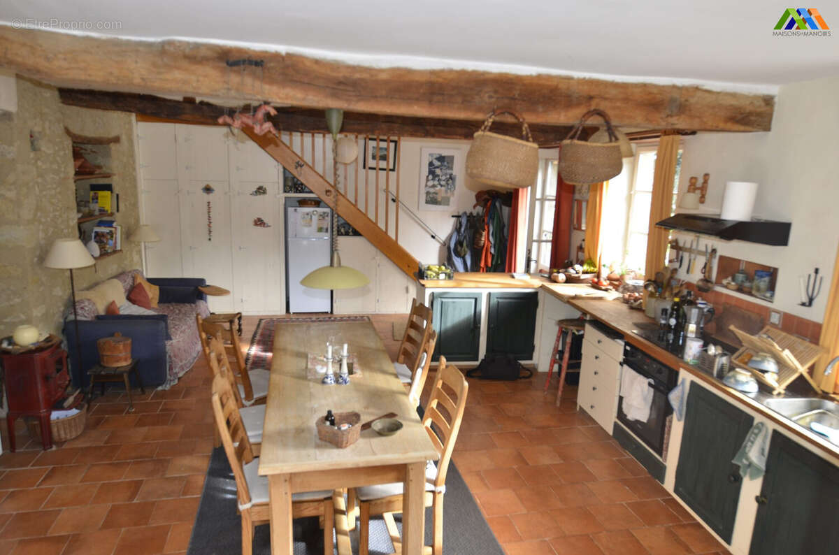 Cuisine rustique dans une maison ancienne avec poutres apparentes et sol en terre cuite.