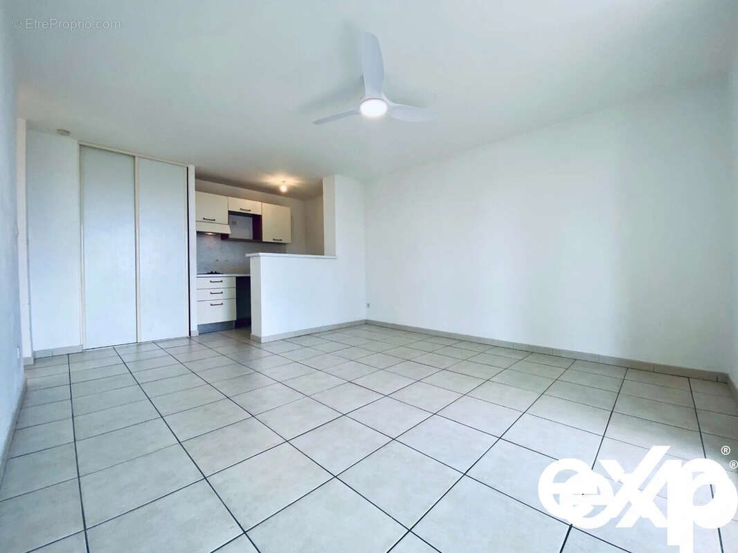 Ceci est une pièce lumineuse avec un sol carrelé, une cuisine ouverte et un plafond avec un ventilateur. - Appartement à SAINT-PAUL