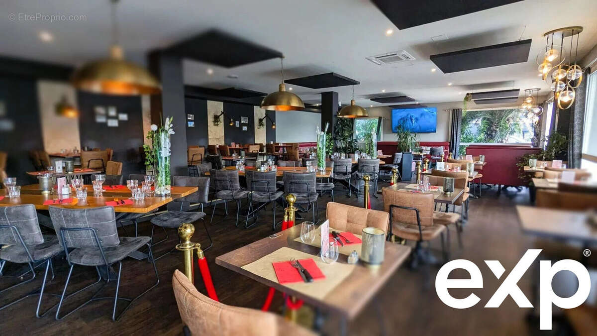 Un intérieur de restaurant moderne avec des tables en bois, des chaises élégantes et des luminaires suspendus. Les tables sont dressées avec des sets de table rouges. - Autre à AGEN