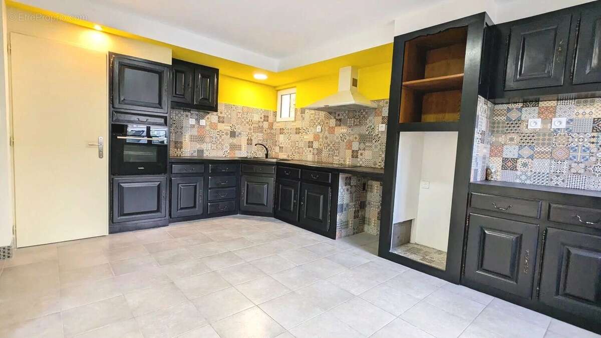 Cuisine avec murs jaunes, tuiles décoratives colorées, et armoires noires. - Maison à DOLMAYRAC