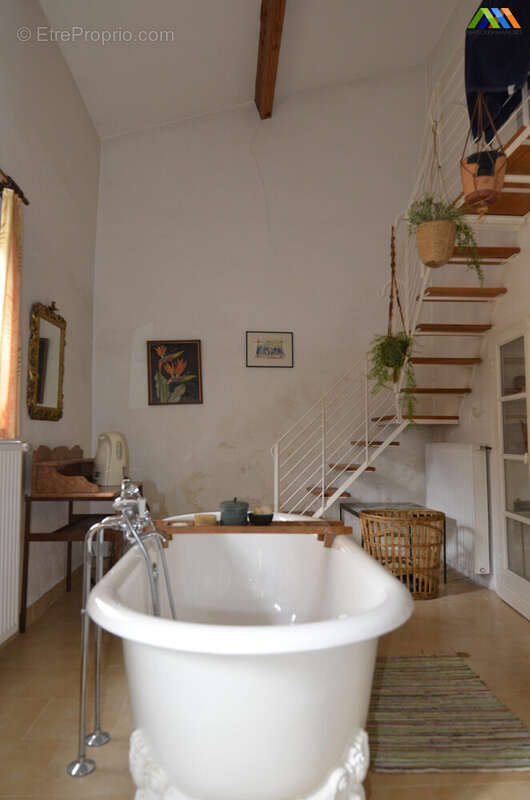 Salle de bain avec baignoire, murs clairs et escalier en bois menant à un niveau supérieur.