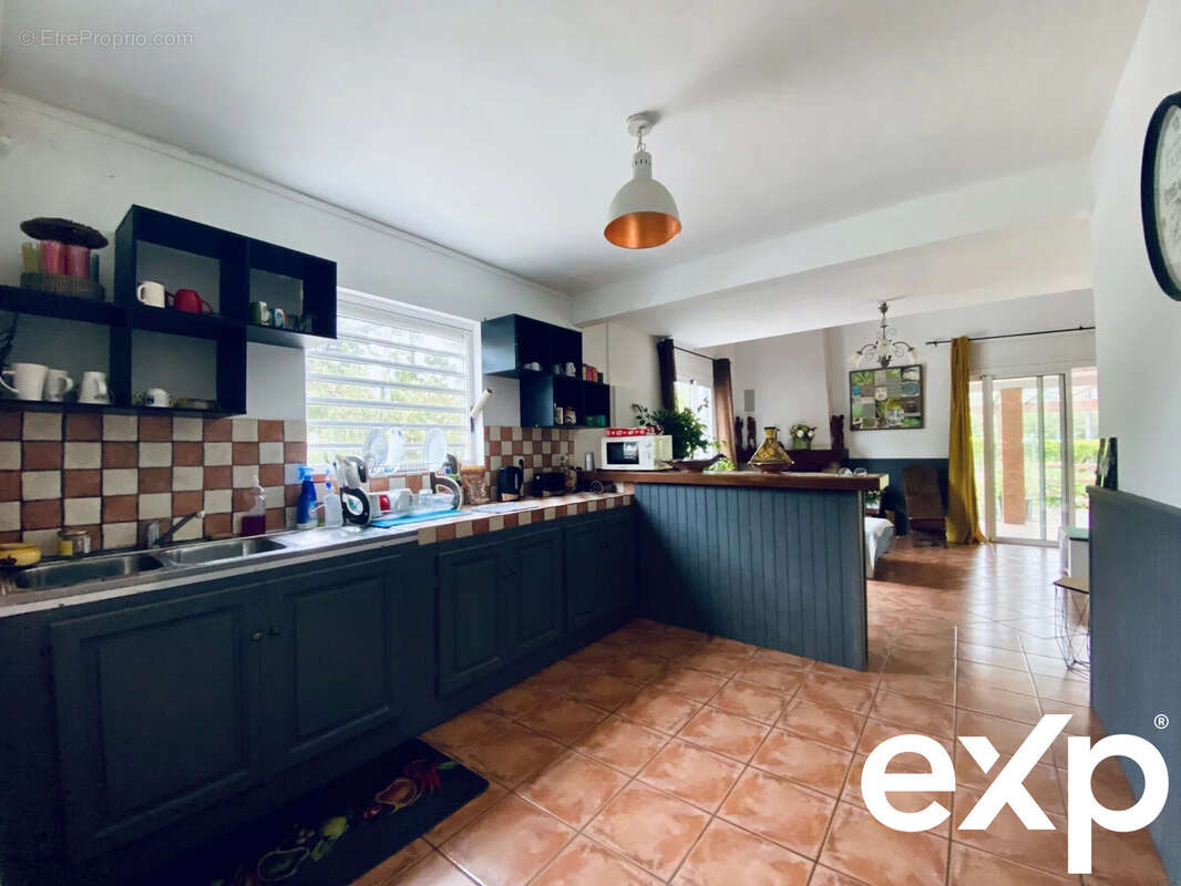 Cuisine spacieuse avec des armoires sombres, un plan de travail en angle, carrelage au sol et des étagères ouvertes. - Maison à LA PLAINE-DES-PALMISTES