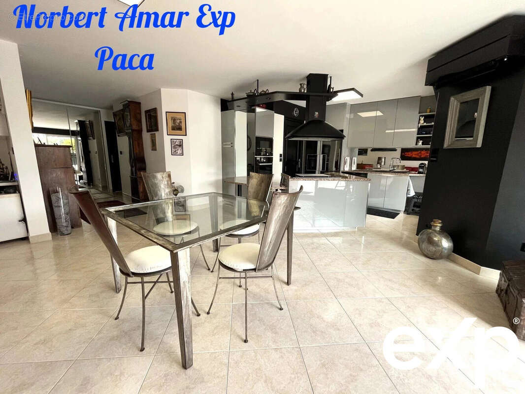 Une cuisine moderne et spacieuse avec un coin repas comprenant une table en verre et des chaises élégantes. Le sol est carrelé et la décoration est contemporaine. - Appartement à FREJUS