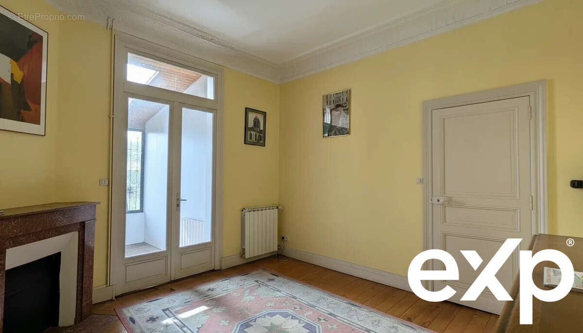 Une pièce lumineuse avec des murs jaunes, une porte-fenêtre donnant sur une véranda et un tapis multicolore sur le sol. - Maison à LE PASSAGE