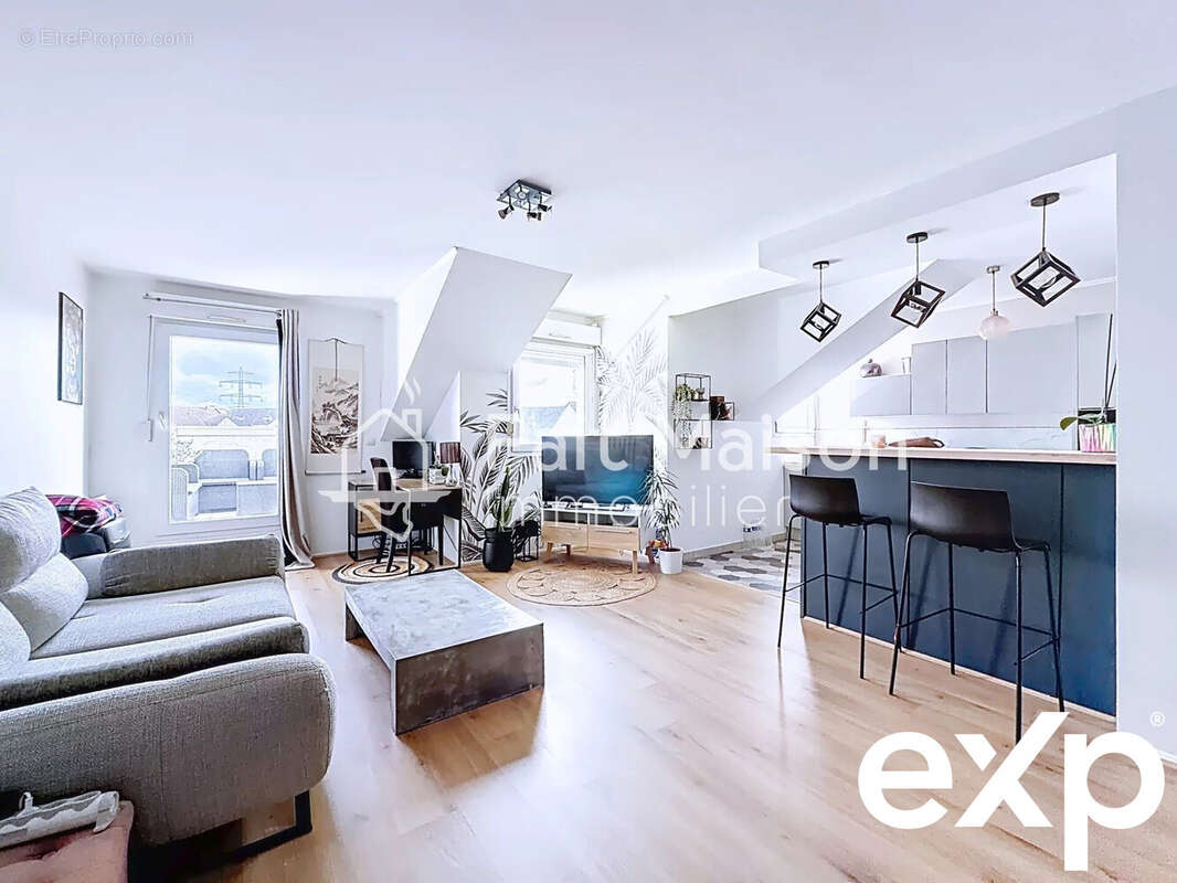 Un salon moderne et lumineux avec un canapé gris, une table basse en bois, un bar à trois chaises hautes, et une cuisine ouverte. - Appartement à MASSY