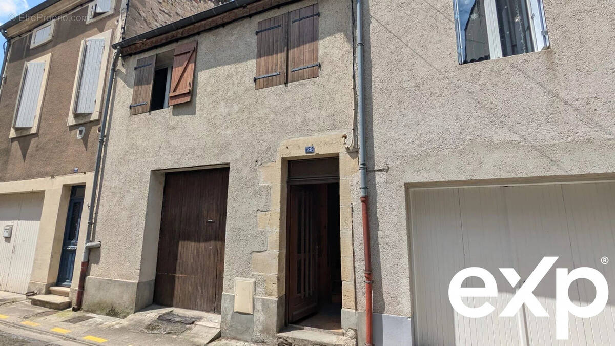Il s'agit d'une façade de maison en pierre avec des volets en bois et un garage marron, située dans une rue résidentielle. - Maison à AGEN