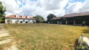 Une grande maison traditionnelle avec un toit en tuiles se trouve à gauche, à côté d'une grange recouverte de lierre à droite, entourée d'une vaste pelouse sous un ciel partiellement nuageux. - Maison à FOULAYRONNES