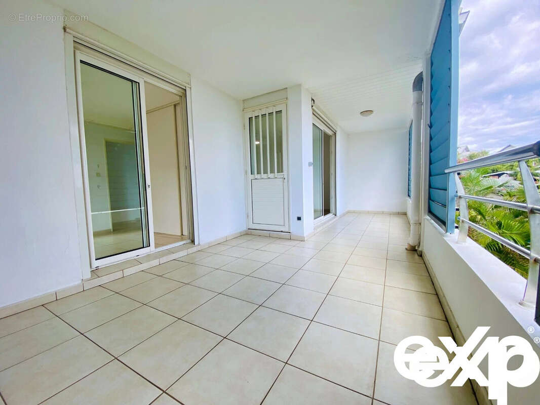 Une terrasse spacieuse en carrelage avec des portes vitrées, offrant une vue dégagée sur l'extérieur. - Appartement à SAINT-PAUL