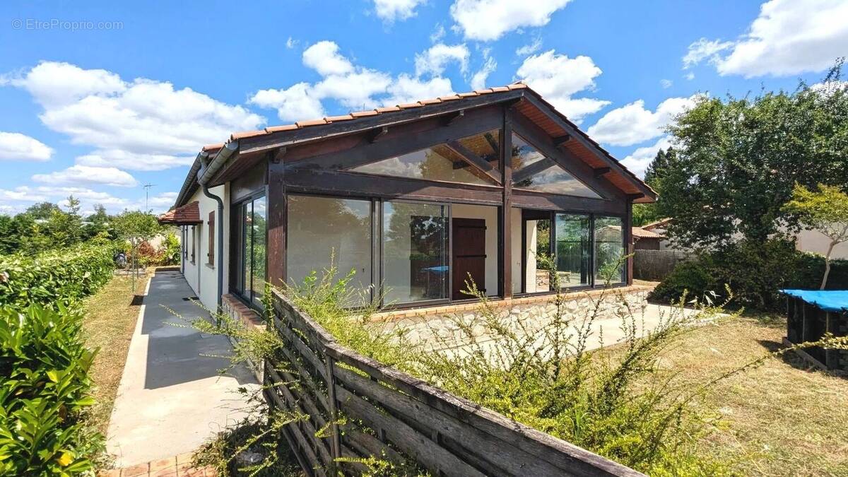 Maison avec de grandes baies vitrées autour de la terrasse, entourée de nature sous un ciel bleu. - Maison à FOULAYRONNES