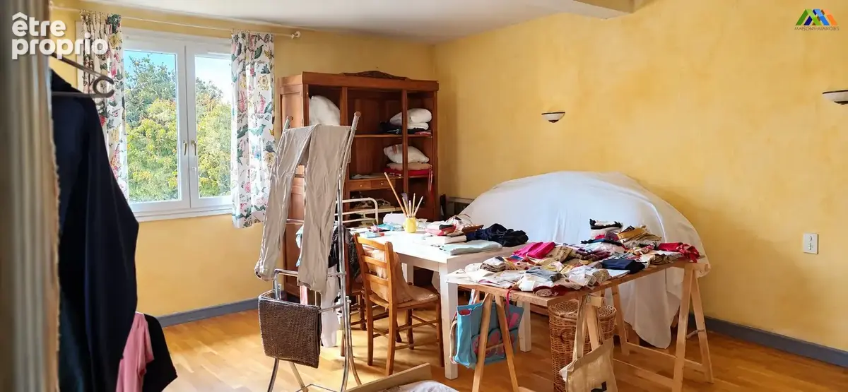 ièce avec parquet, murs jaunes et fenêtre sur les arbres, aménagée avec des tables de travail et une armoire.