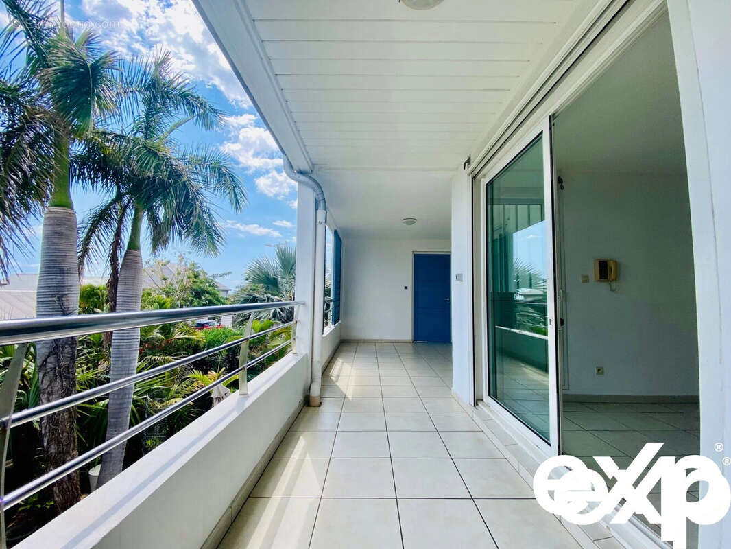 Une terrasse spacieuse avec vue sur des palmiers, dotée de grandes baies vitrées coulissantes. - Appartement à SAINT-PAUL
