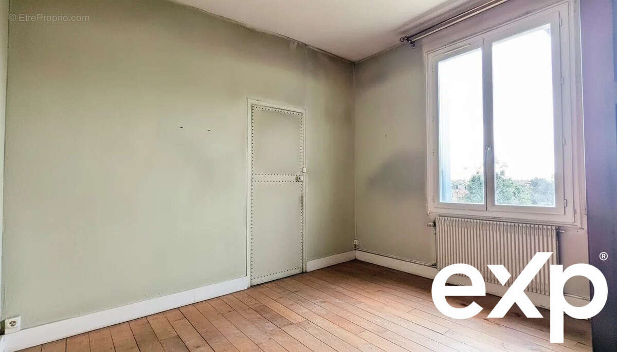 Une pièce vide avec un sol en bois, un mur vert, une porte et une grande fenêtre à côté d'un radiateur. - Maison à LE PASSAGE