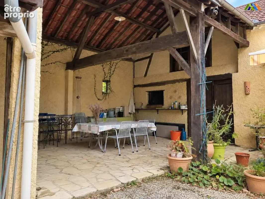 Une terrasse de repas couverte sous une charpente en bois apparente.