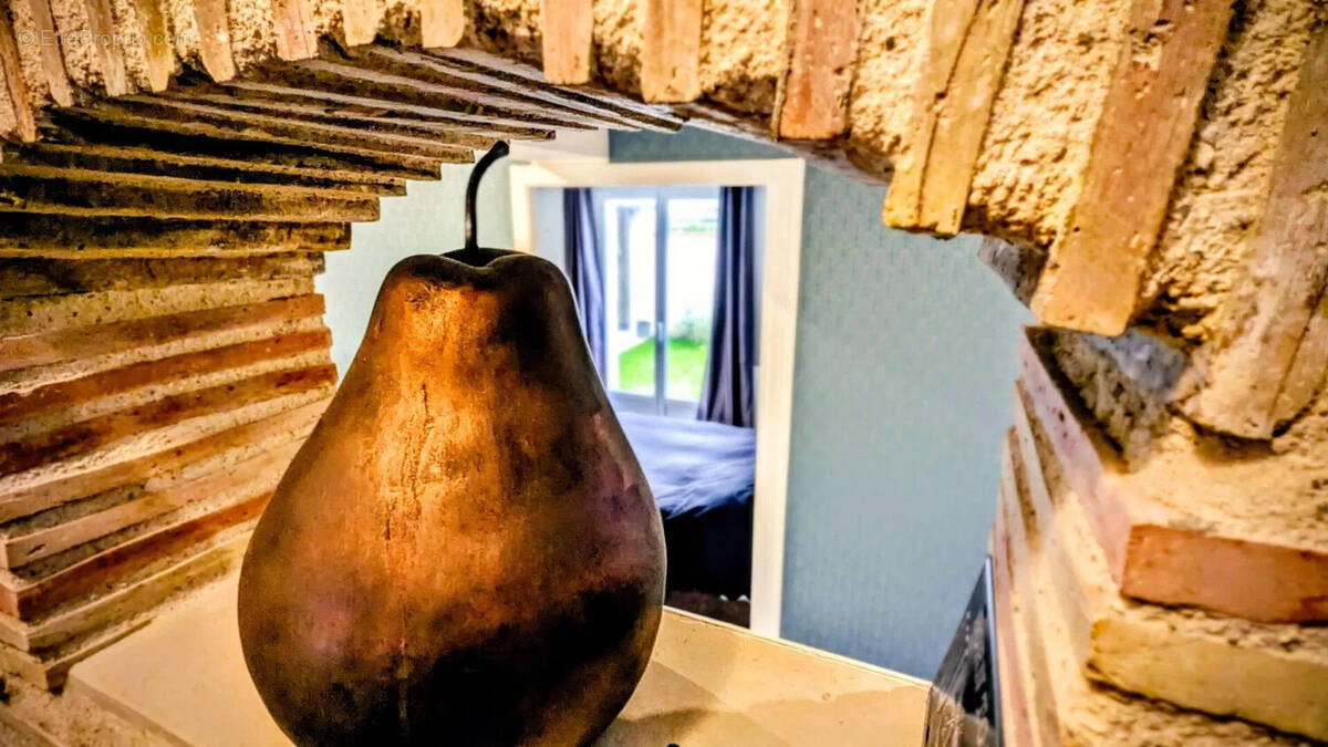 Un cadre en brique entoure une sculpture en forme de poire avec une fenêtre en arrière-plan. - Maison à AIGUILLON