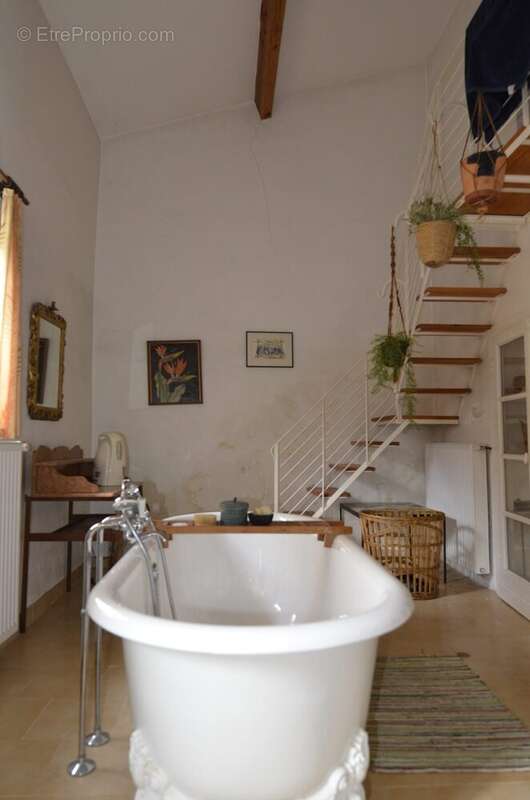 Salle de bain avec baignoire, murs clairs et escalier en bois menant à un niveau supérieur. - Maison à BASSOUES