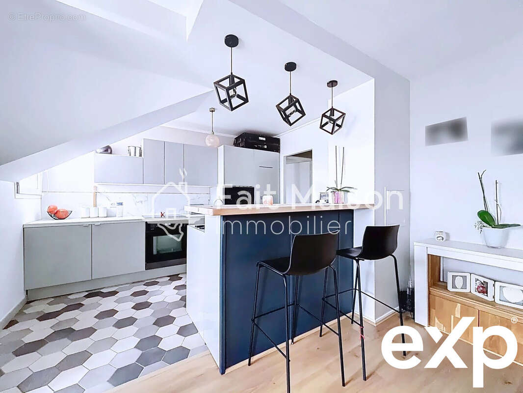 Cuisine moderne avec îlot central, chaises hautes et luminaires suspendus, sol en carrelage hexagonal et parquet. - Appartement à MASSY