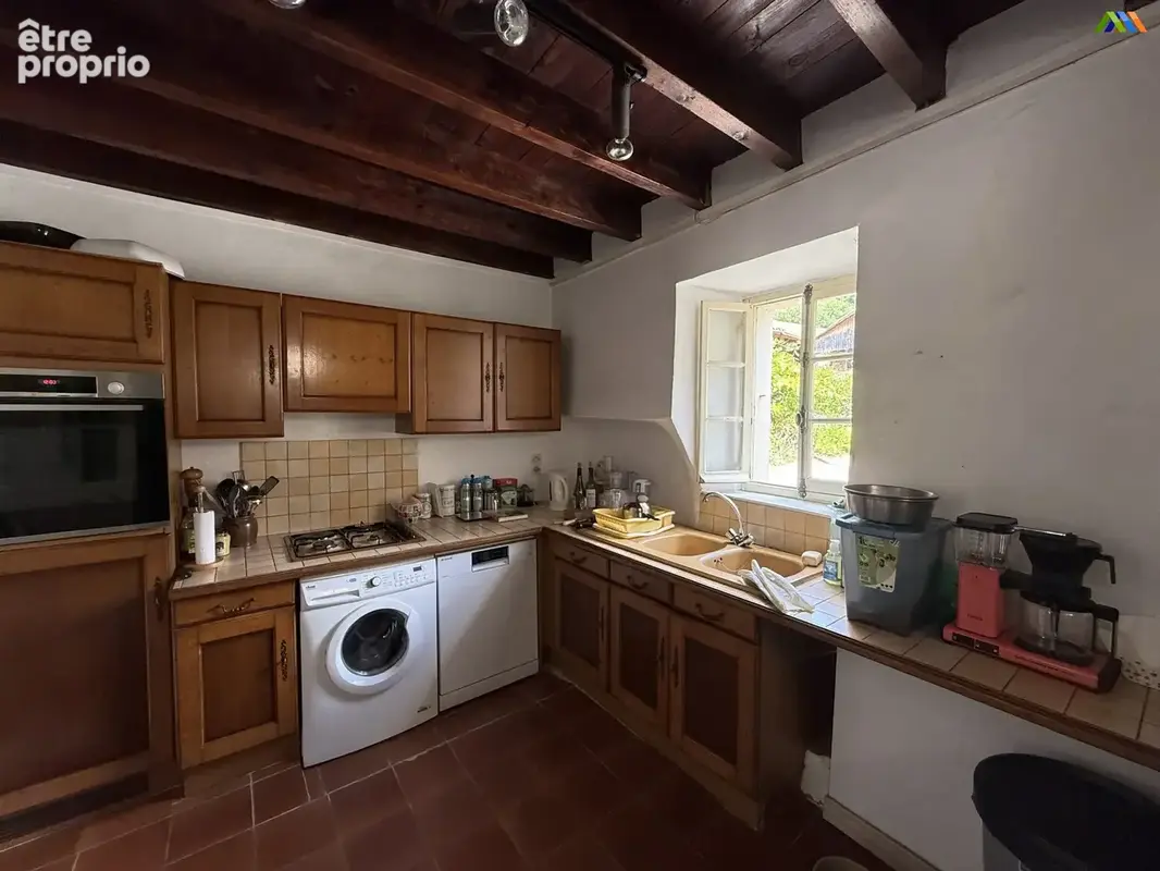 Cuisine de style traditionnel avec poutres apparentes, rangements en bois et équipements pratiques.