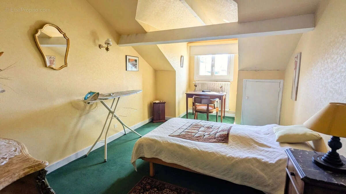 Une chambre lumineuse avec des murs jaunes, un lit simple, un fer à repasser sur sa table, et un bureau près d'une fenêtre. - Maison à FOULAYRONNES