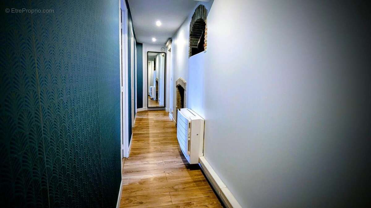 Un couloir étroit avec un sol en bois, des murs blancs et un mur latéral bleu foncé, bien éclairé et décoré d'un radiateur mural. - Maison à AIGUILLON