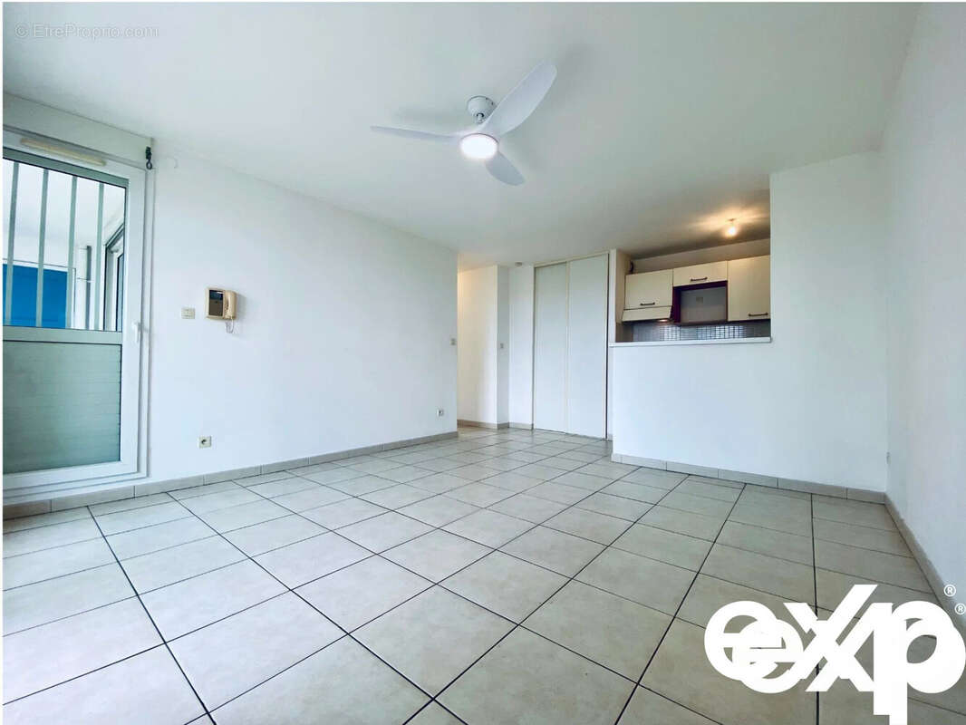 Une pièce lumineuse avec carrelage au sol, un ventilateur de plafond, et une cuisine ouverte. - Appartement à SAINT-PAUL