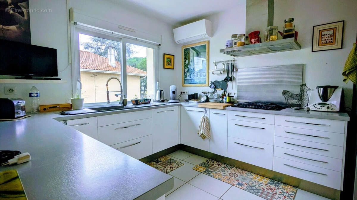 Une cuisine moderne et lumineuse avec des armoires blanches, des étagères ouvertes, et une fenêtre donnant sur l'extérieur. - Maison à AIGUILLON