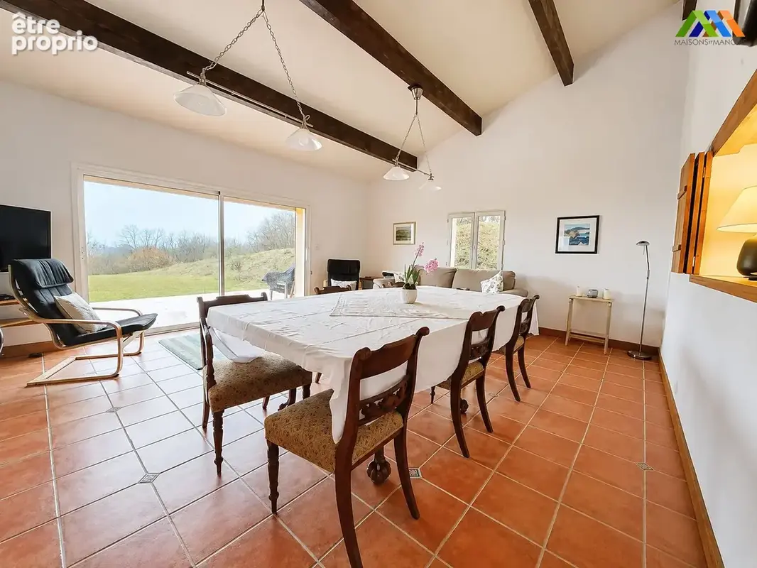Salle à manger lumineuse avec poutres apparentes et accès direct au jardin.