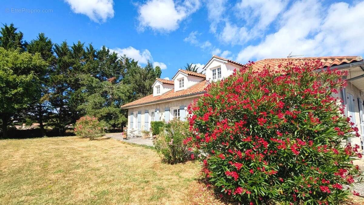 Une maison avec un toit en tuiles entourée de verdure et de buissons fleuris sous un ciel bleu. - Maison à FOULAYRONNES