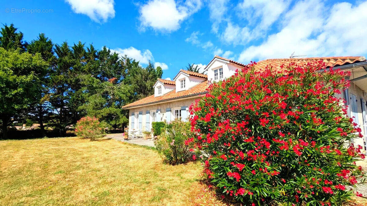 Une maison avec un toit en tuiles entourée de verdure et de buissons fleuris sous un ciel bleu. - Maison à FOULAYRONNES