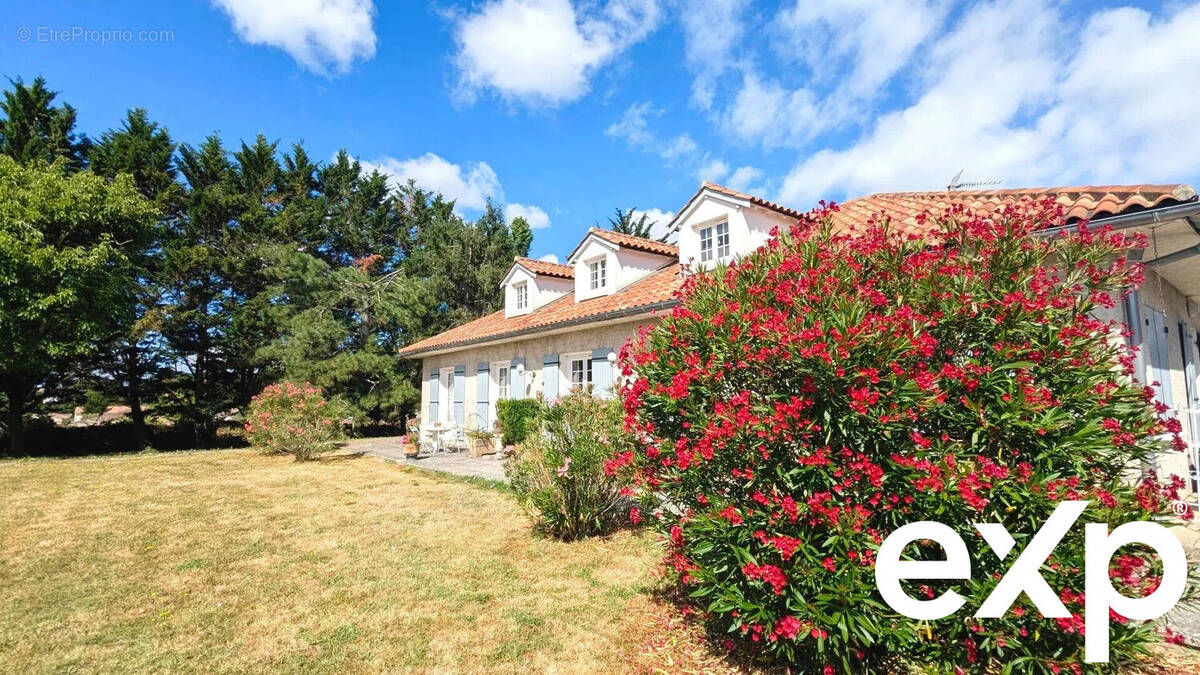 Une maison avec un toit en tuiles entourée de verdure et de buissons fleuris sous un ciel bleu. - Maison à FOULAYRONNES