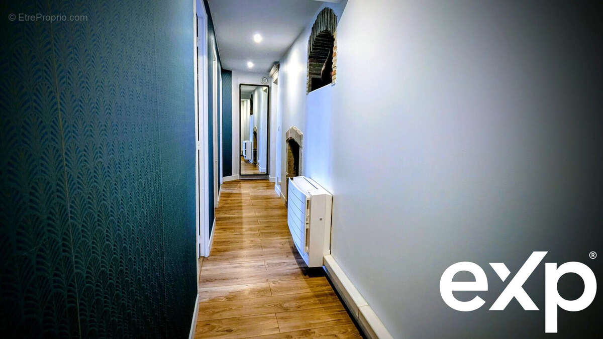 Un couloir étroit avec un sol en bois, des murs blancs et un mur latéral bleu foncé, bien éclairé et décoré d'un radiateur mural. - Maison à AIGUILLON