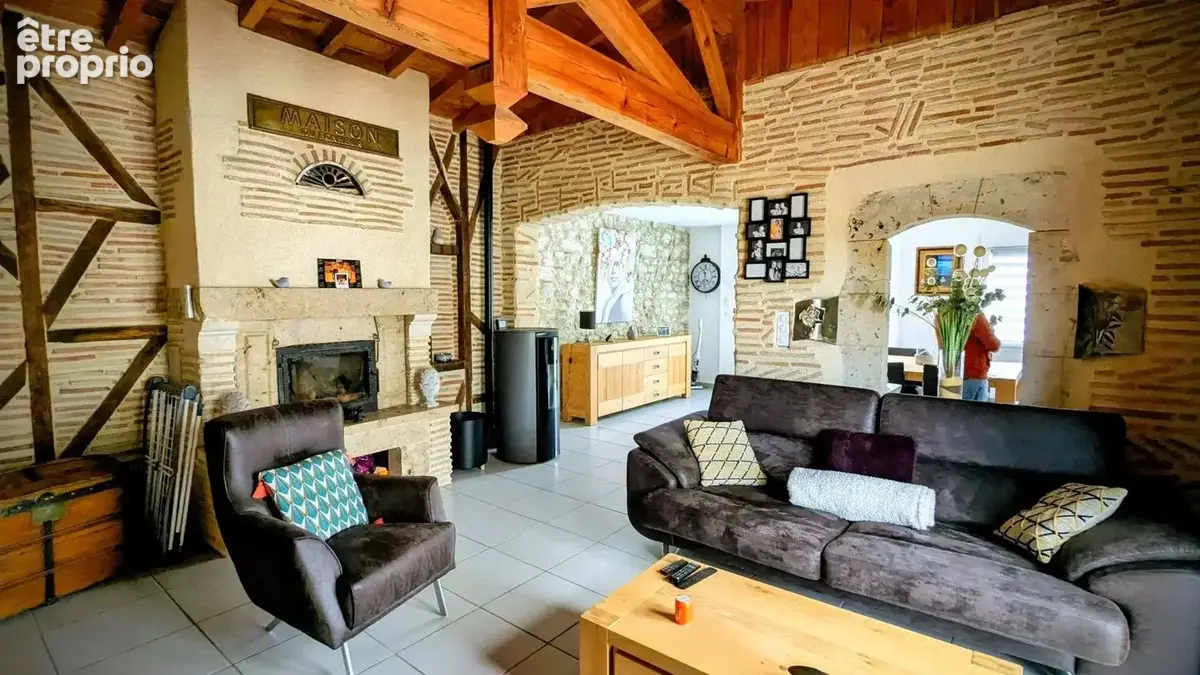 Salon chaleureux avec murs à colombages, poutres apparentes, cheminée, et mobilier confortable.