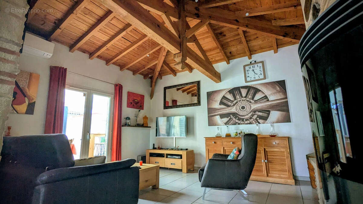 Un salon avec un plafond en bois, des meubles modernes, et des oeuvres d'art murales. - Maison à AIGUILLON