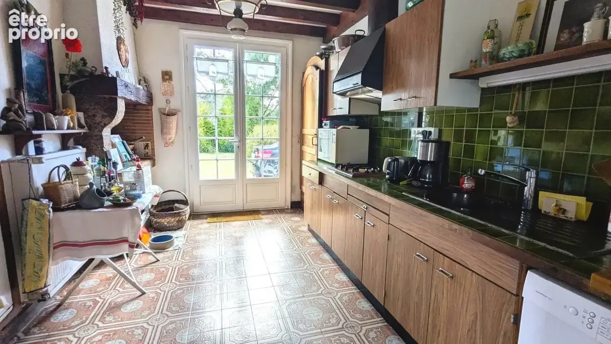 Une cuisine rustique avec des éléments en bois, des carreaux de céramique au sol, des portes vitrées menant à l'extérieur et un plan de travail avec des appareils électroménagers.