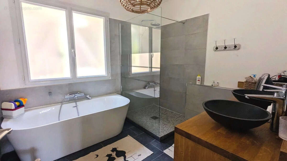 Une salle de bain moderne avec une baignoire, une douche vitrée et un lavabo noir sur un meuble en bois. - Maison à FOULAYRONNES