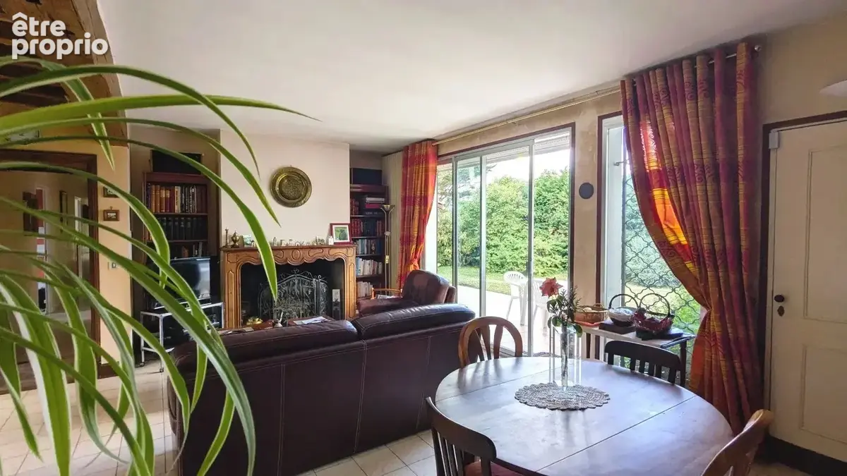 Un salon confortable avec une cheminée, des canapés en cuir, une table à manger en bois et de grandes fenêtres donnant sur un jardin.
