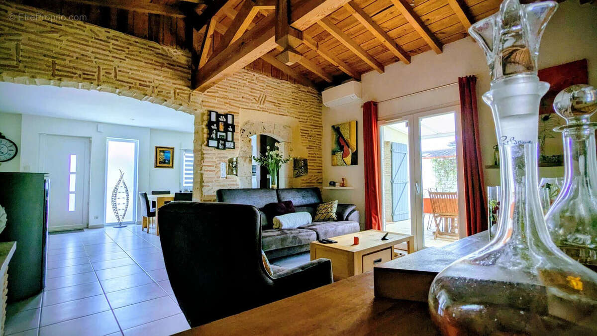Un salon chaleureux avec un plafond en bois, une lumière naturelle abondante, et une décoration élégante. - Maison à AIGUILLON