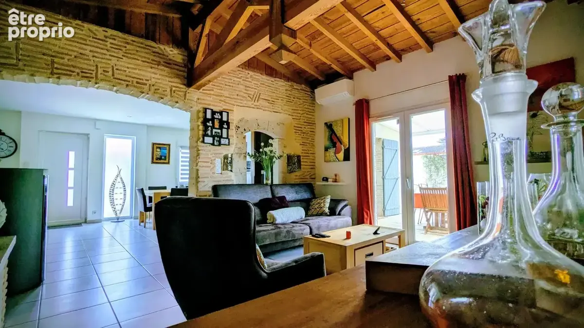 Un salon chaleureux avec un plafond en bois, une lumière naturelle abondante, et une décoration élégante.