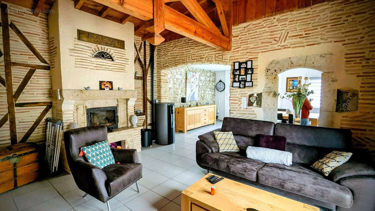 Salon chaleureux avec murs à colombages, poutres apparentes, cheminée, et mobilier confortable. - Maison à AIGUILLON