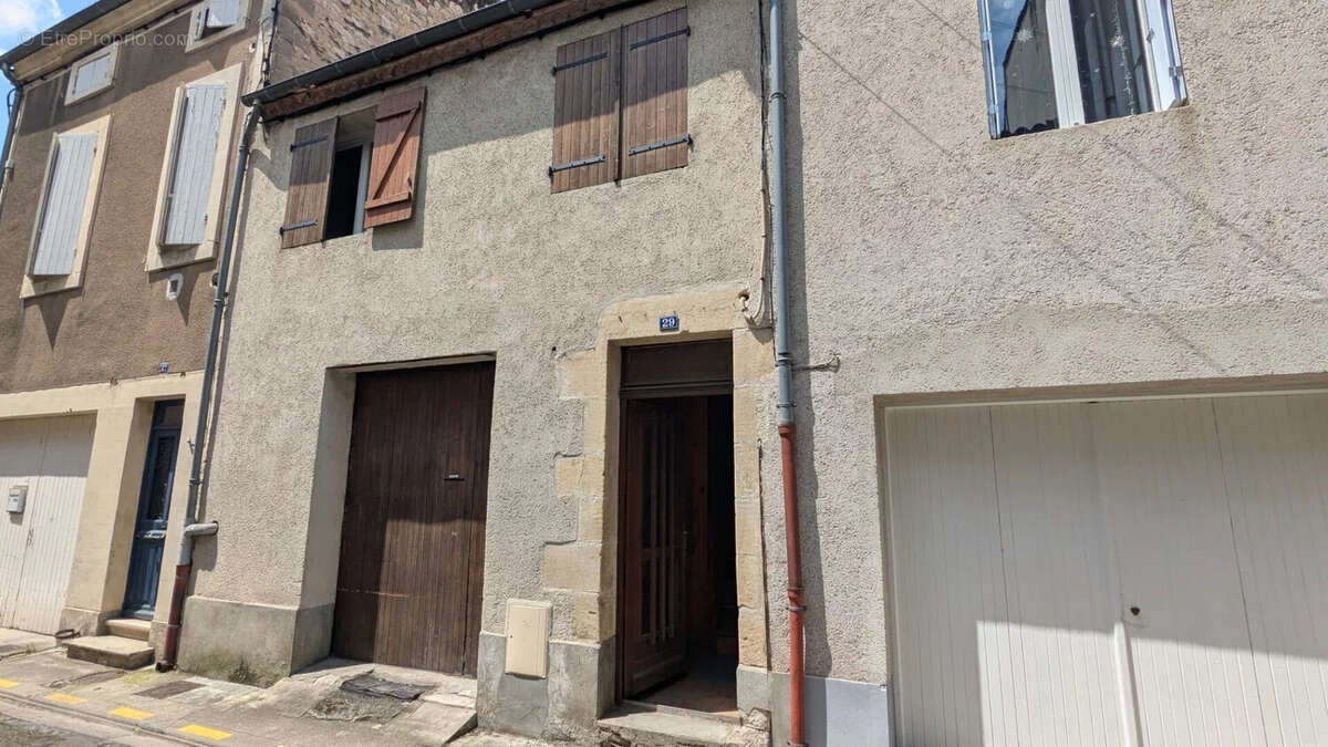 Il s'agit d'une façade de maison en pierre avec des volets en bois et un garage marron, située dans une rue résidentielle. - Maison à AGEN