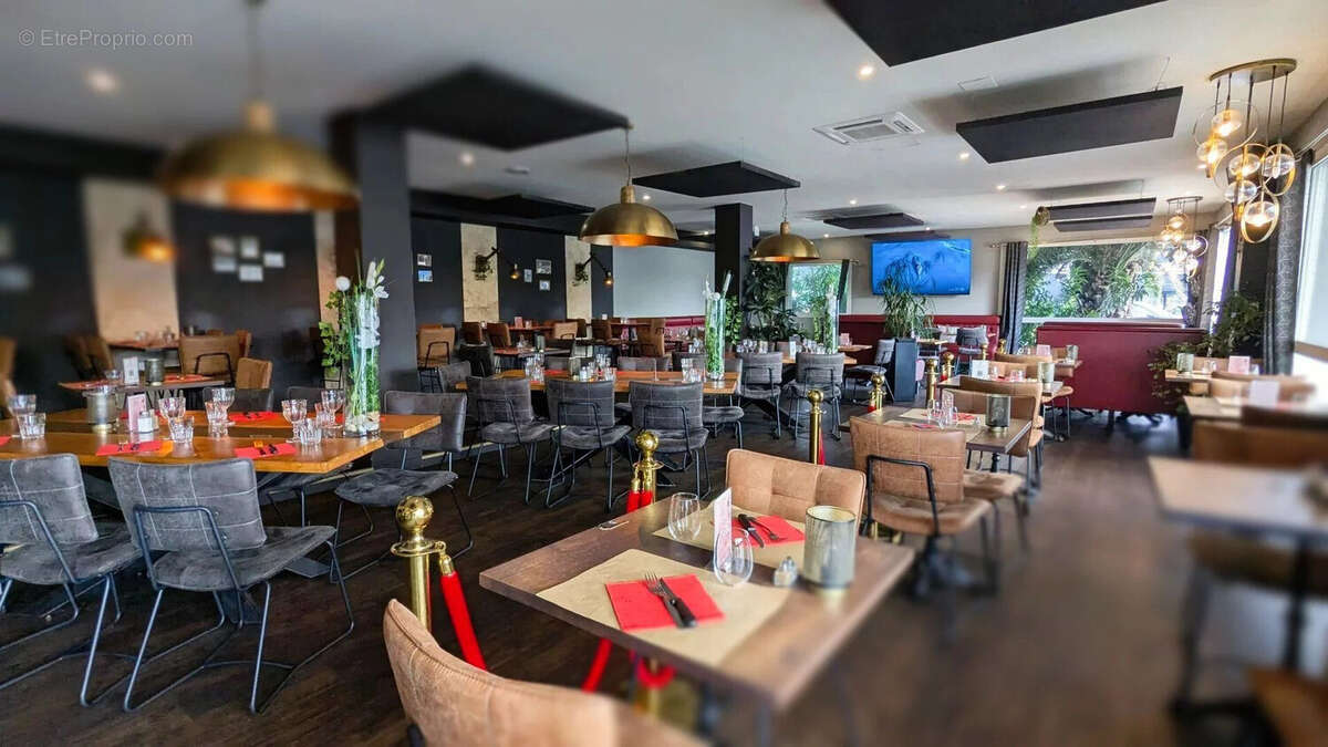 Un intérieur de restaurant moderne avec des tables en bois, des chaises élégantes et des luminaires suspendus. Les tables sont dressées avec des sets de table rouges. - Autre à AGEN