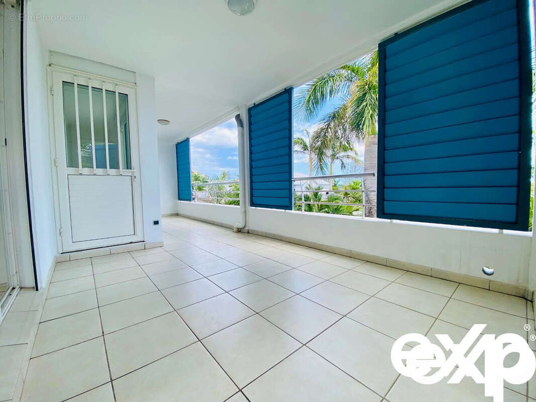 Une terrasse spacieuse avec des stores bleus et une vue sur des palmiers. - Appartement à SAINT-PAUL