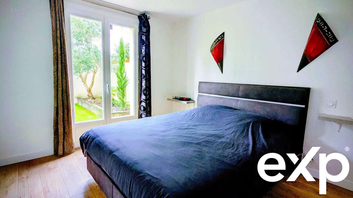 Une chambre moderne avec un lit double, des décorations murales rouges, avec ouverture donnant sur un jardin. - Maison à AIGUILLON