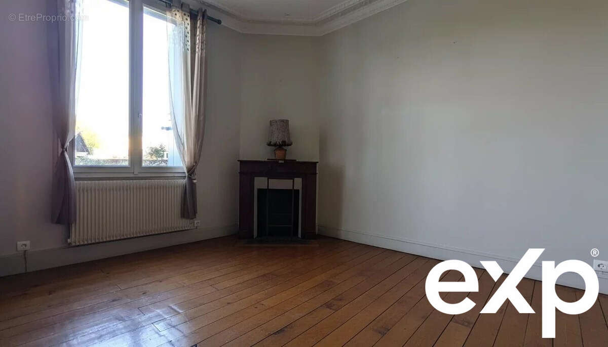 Une pièce vide avec un parquet en bois, une fenêtre avec des rideaux et une cheminée agrémentée d'une lampe. - Maison à LE PASSAGE